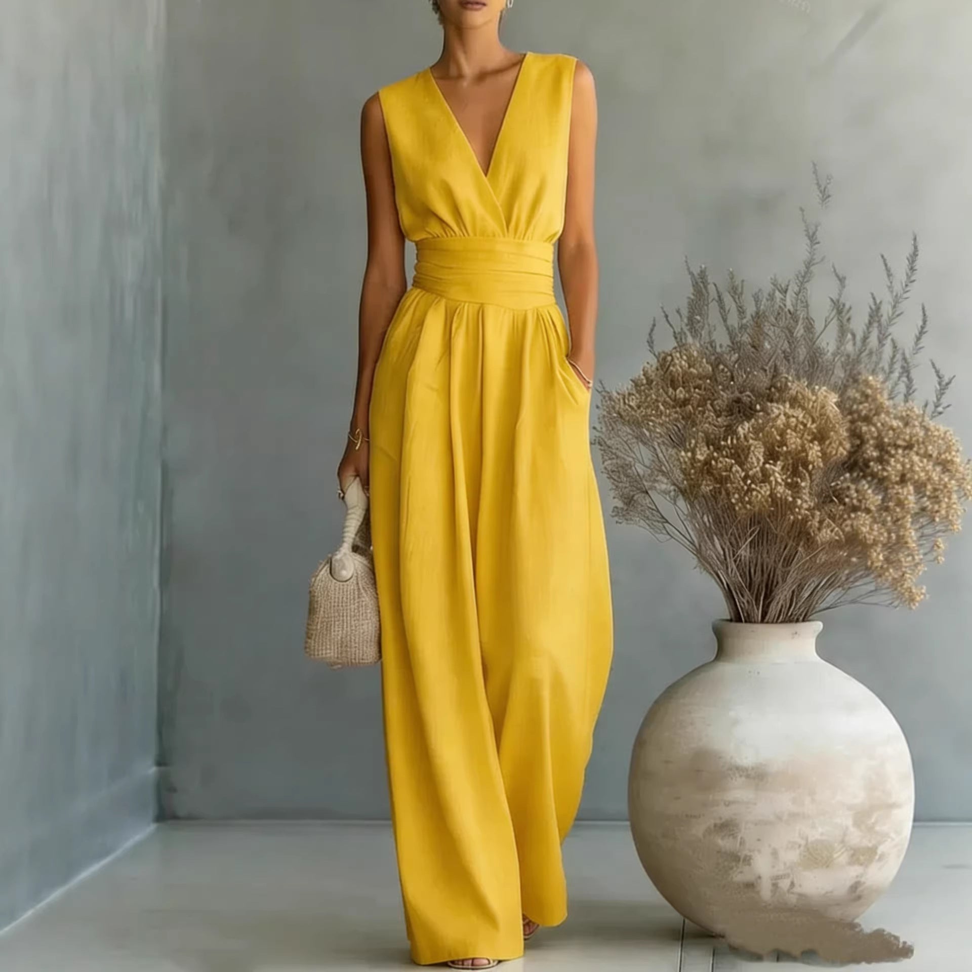 Woman in a yellow dress standing next to a vase with dried flowers indoors.