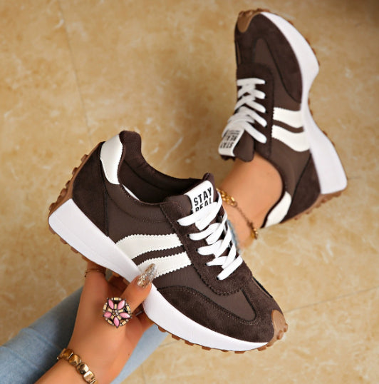 Brown and white sneakers being held up against a beige background