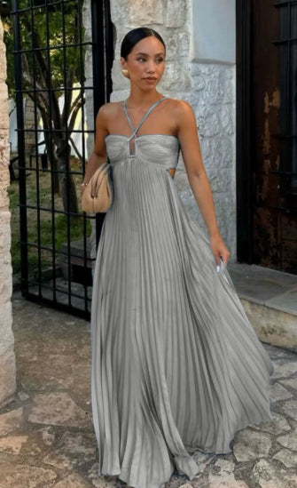 Woman in a silver pleated dress standing outdoors near a stone wall.