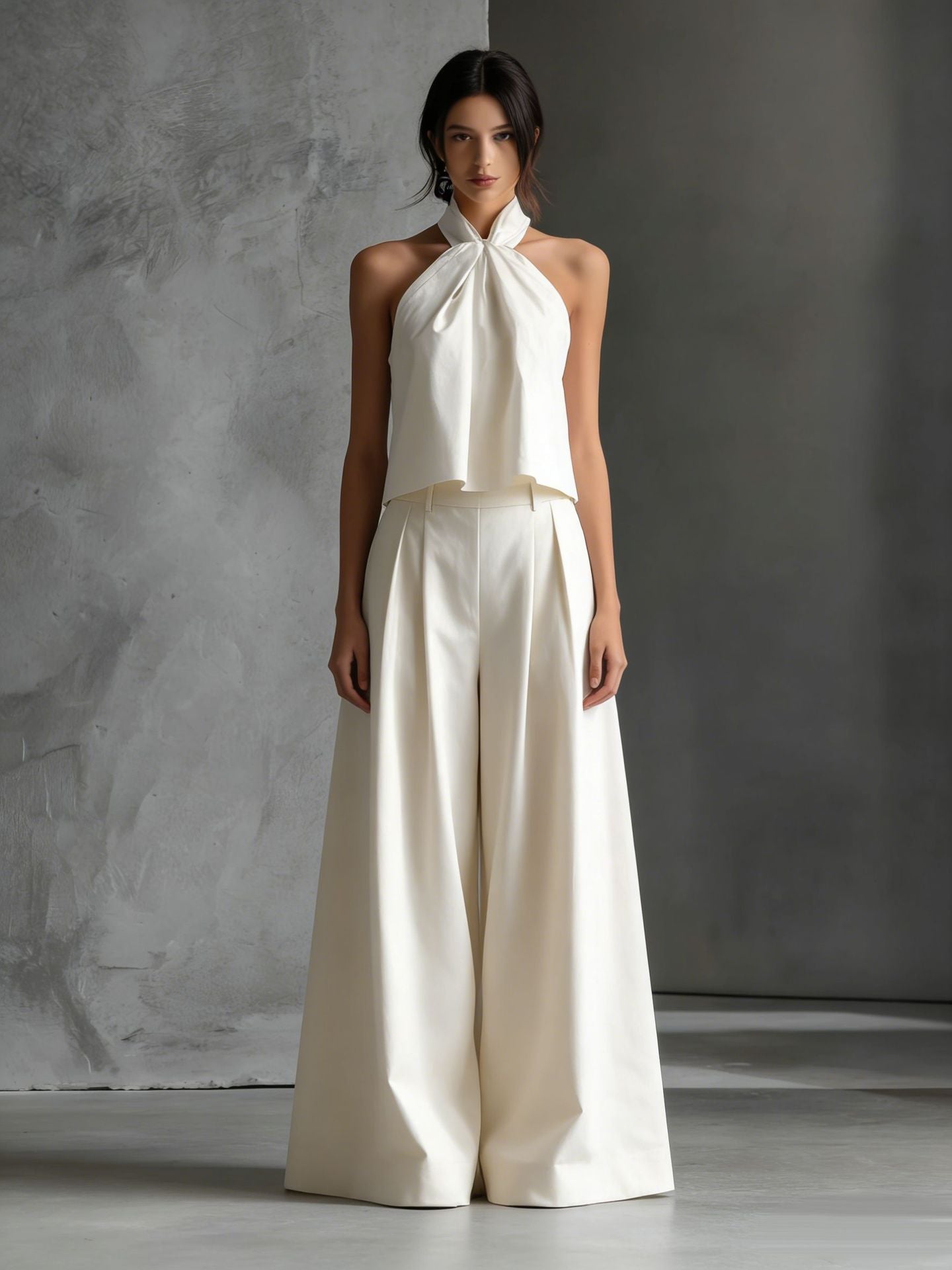 Woman wearing a white halter top and wide-leg pants against a gray background