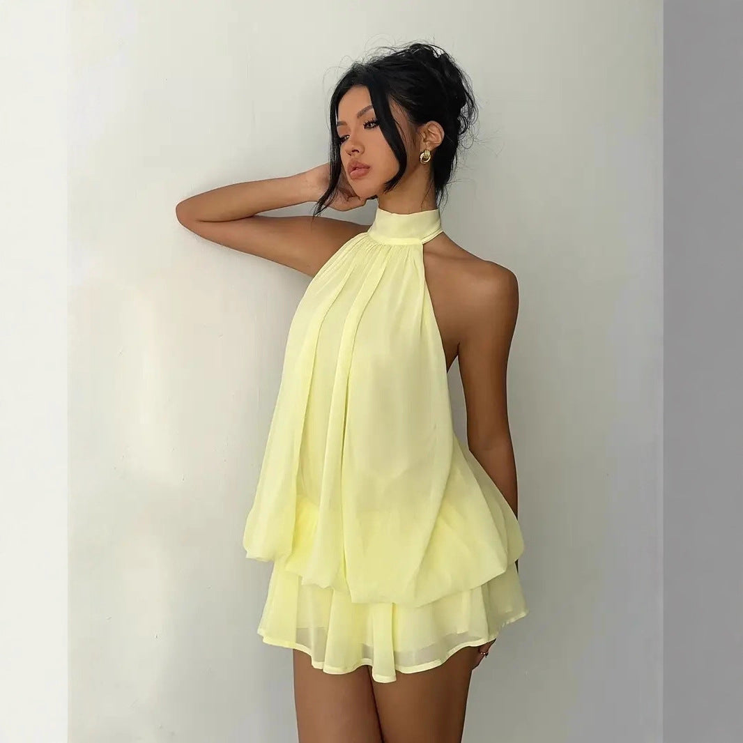 Woman wearing a light yellow halter neck dress against a plain background