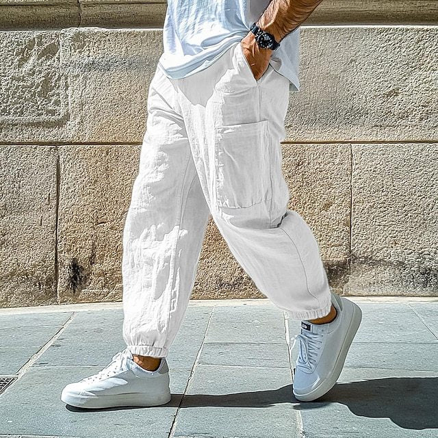 Person wearing white pants and sneakers in front of a stone wall.