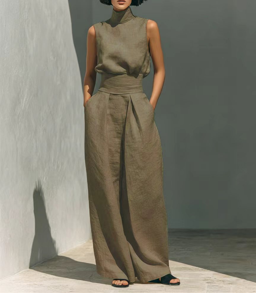 Person wearing a green sleeveless top and wide-leg pants against a gray wall.