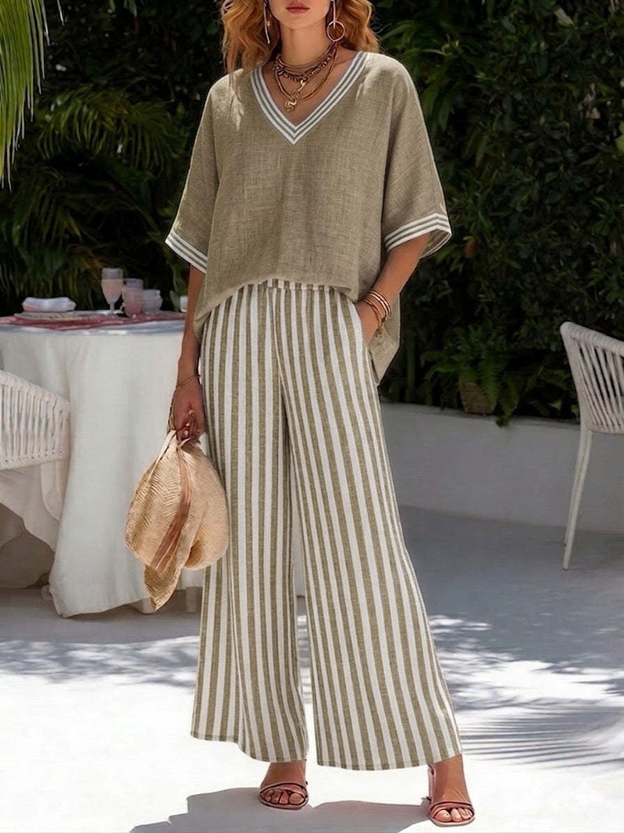 Woman wearing a beige top and striped pants standing outdoors with greenery in the background.