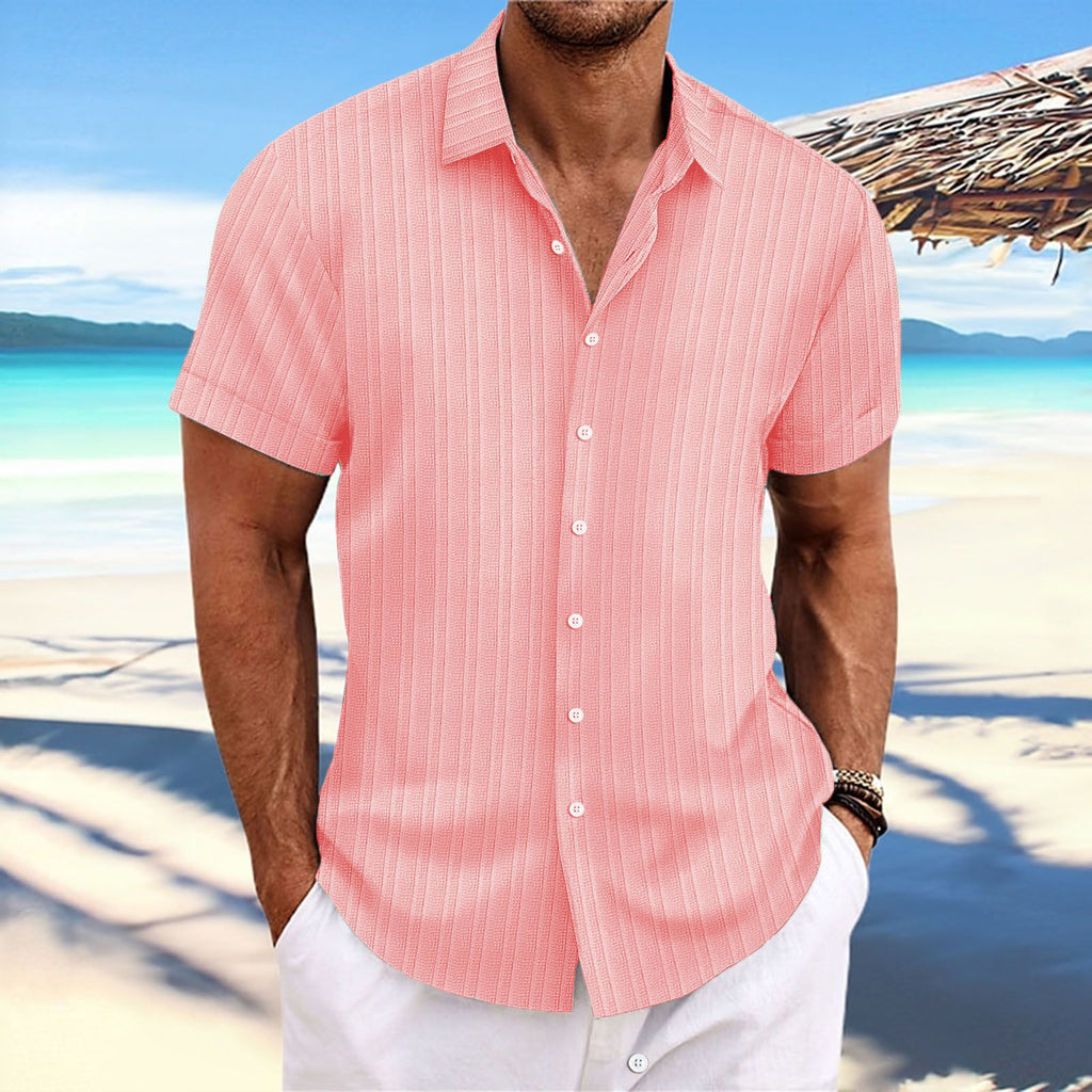 Man wearing a pink striped shirt on a beach with a scenic background