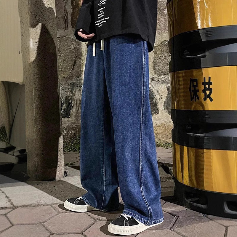 Person wearing blue jeans and black shoes standing next to a yellow and black barrel on a stone pavement.