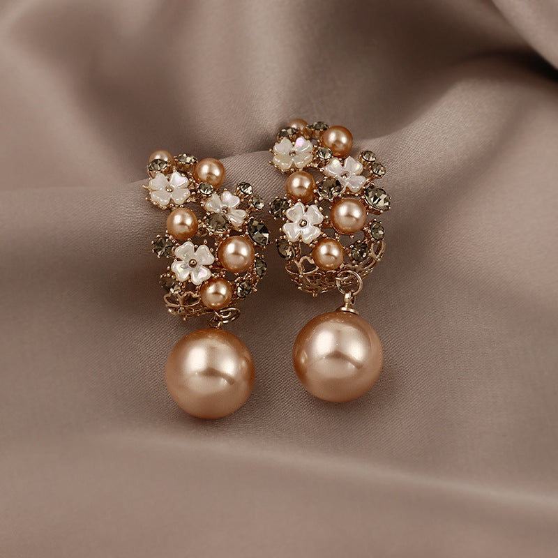 Pair of pearl earrings with floral designs on a brown fabric background