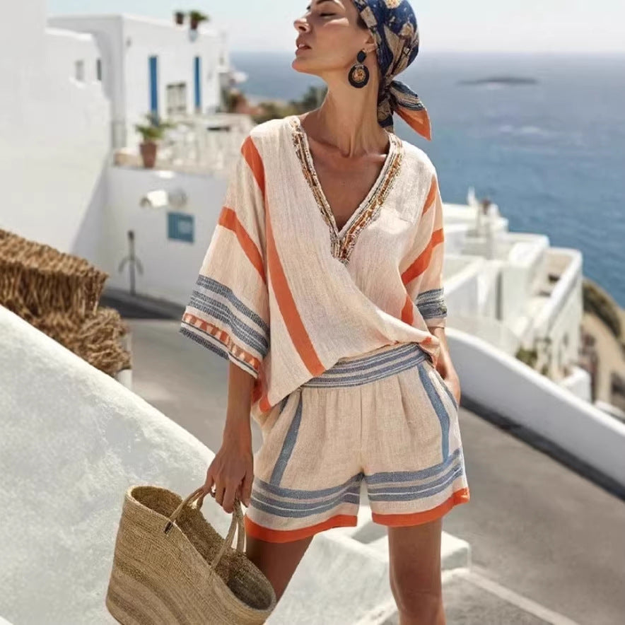 Woman in a colorful outfit with a headscarf and shorts, standing on a balcony with ocean view.