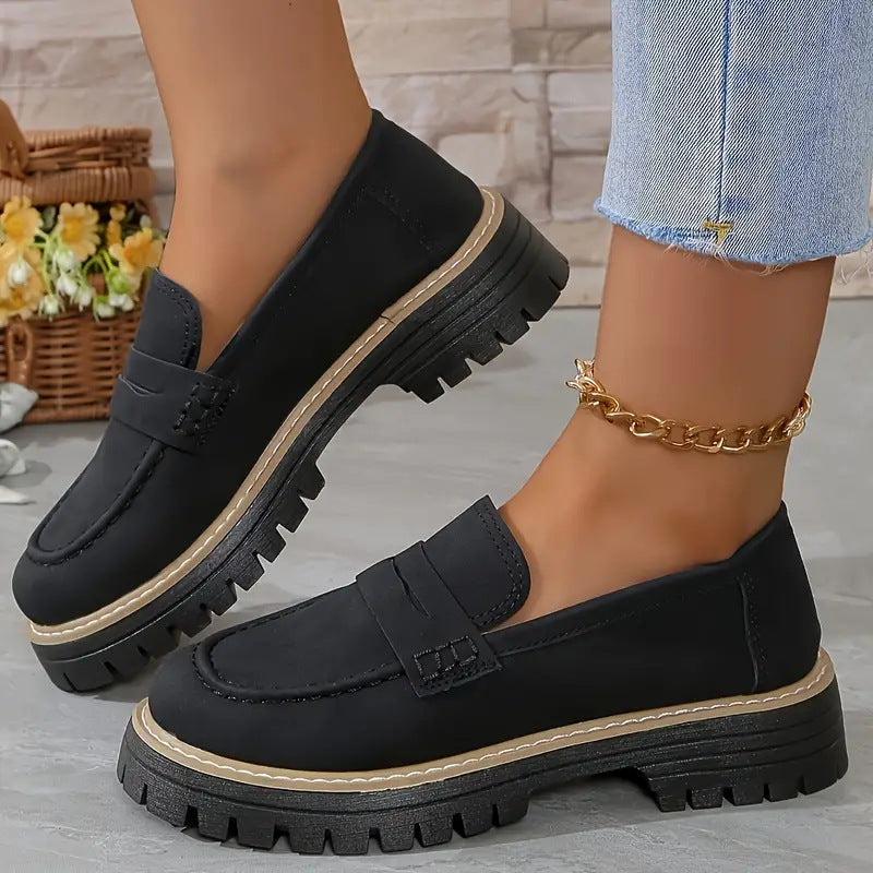 Black loafers worn with denim jeans on a light background