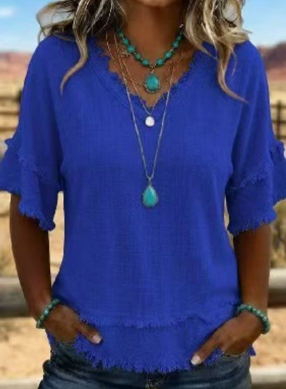Person wearing a blue top with ruffled sleeves and layered necklaces outdoors.