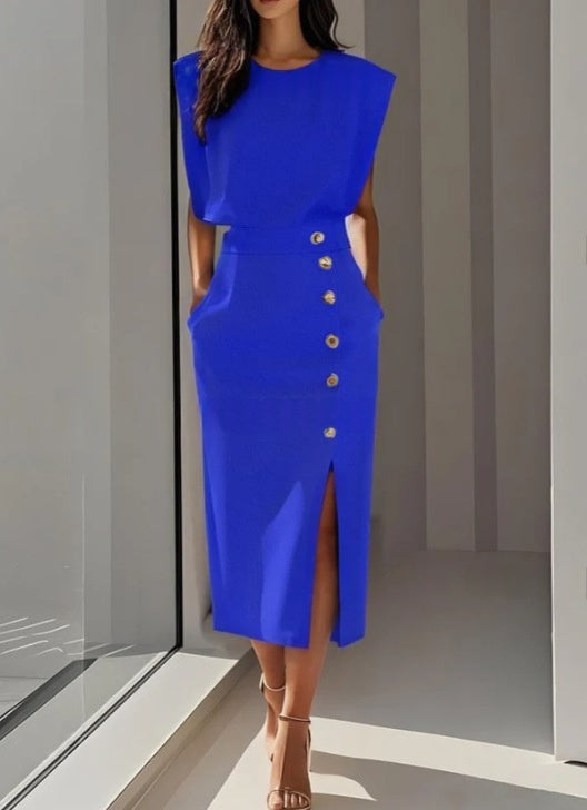 Woman wearing a blue dress with gold buttons in a minimal indoor setting