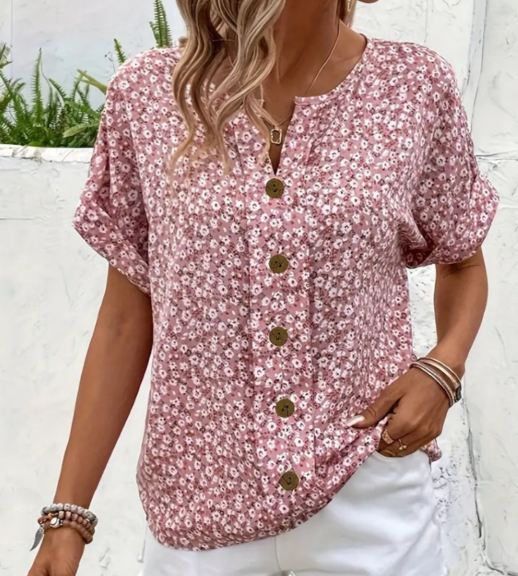 Woman wearing a pink floral blouse with buttons against a white wall.
