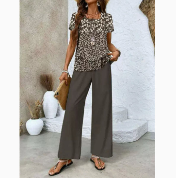 Woman wearing a patterned top and wide-leg pants in a minimalistic setting.