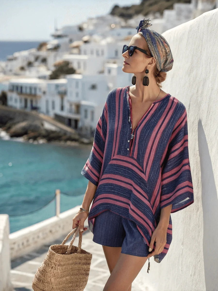 Woman in a striped cover-up standing on a balcony with a scenic view of a coastal town.