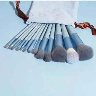 Set of blue makeup brushes with gray bristles and white pouch on light blue surface