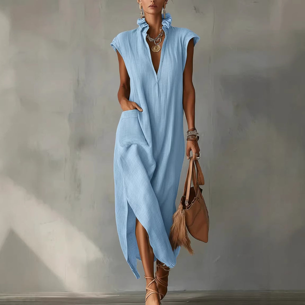 Woman wearing a light blue sleeveless dress holding a brown handbag against a plain background