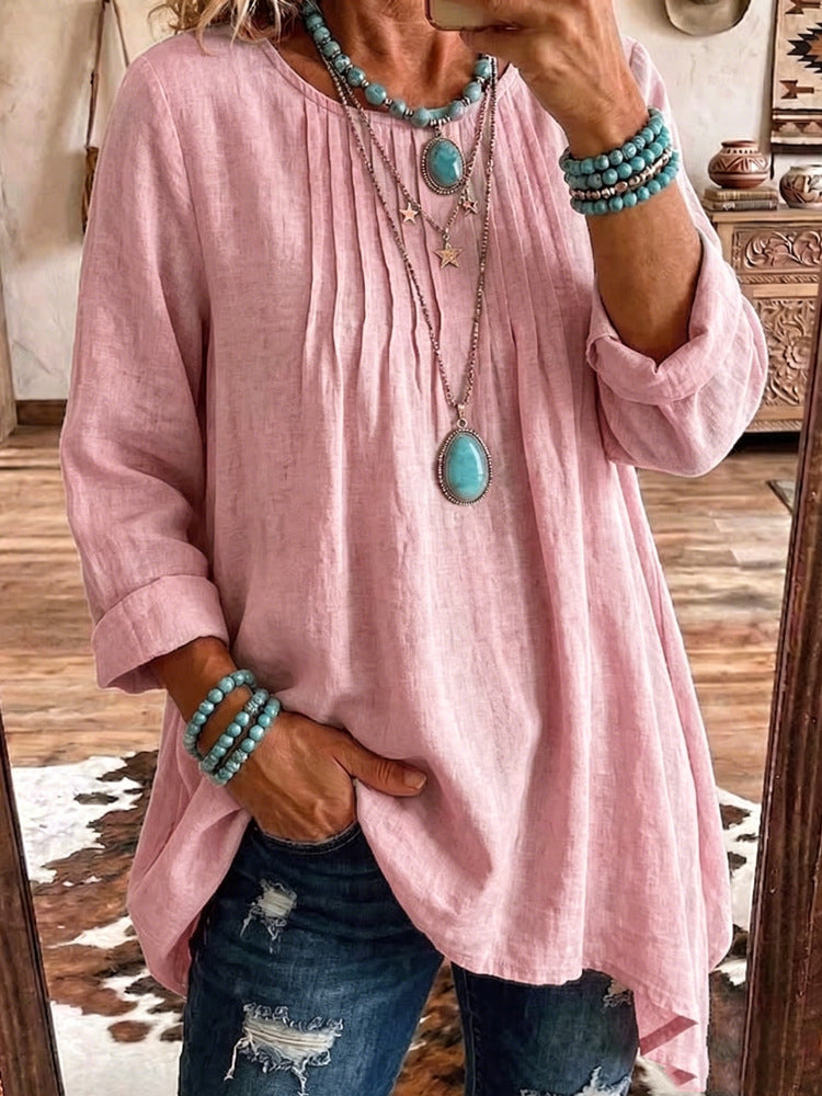 A woman takes a mirror selfie wearing a loose, dusty pink linen-blend tunic top with three-quarter sleeves, paired with distressed blue jeans and turquoise jewelry.