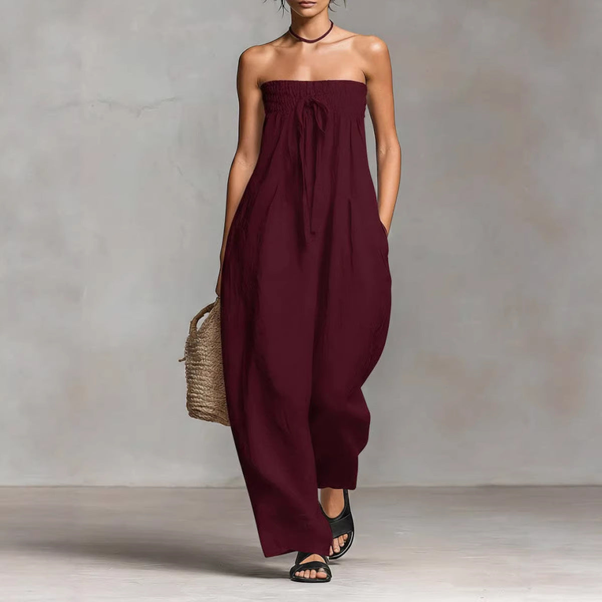 Woman wearing a strapless burgundy jumpsuit against a neutral background