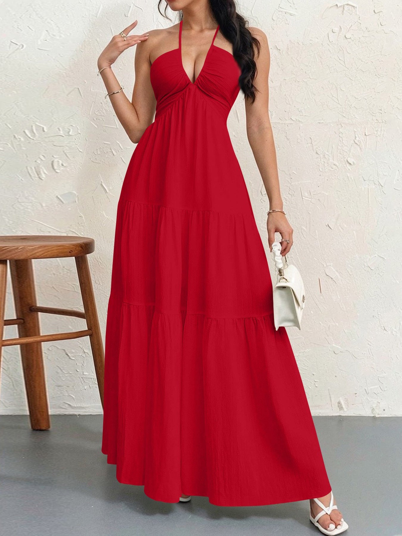 Woman wearing a red halter neck dress against a white wall.