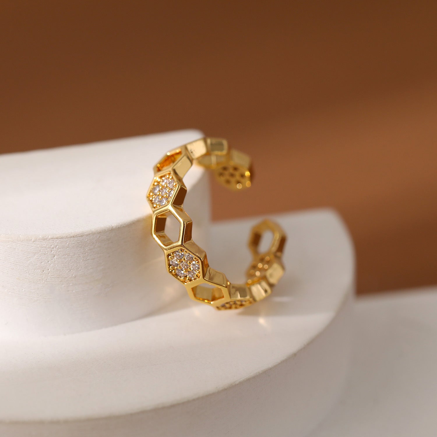 Gold ring with honeycomb design and embedded stones on a white stand with a brown background