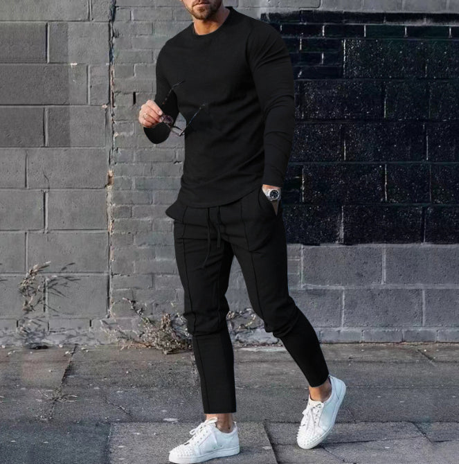 Man wearing a black outfit with white sneakers standing against a brick wall.