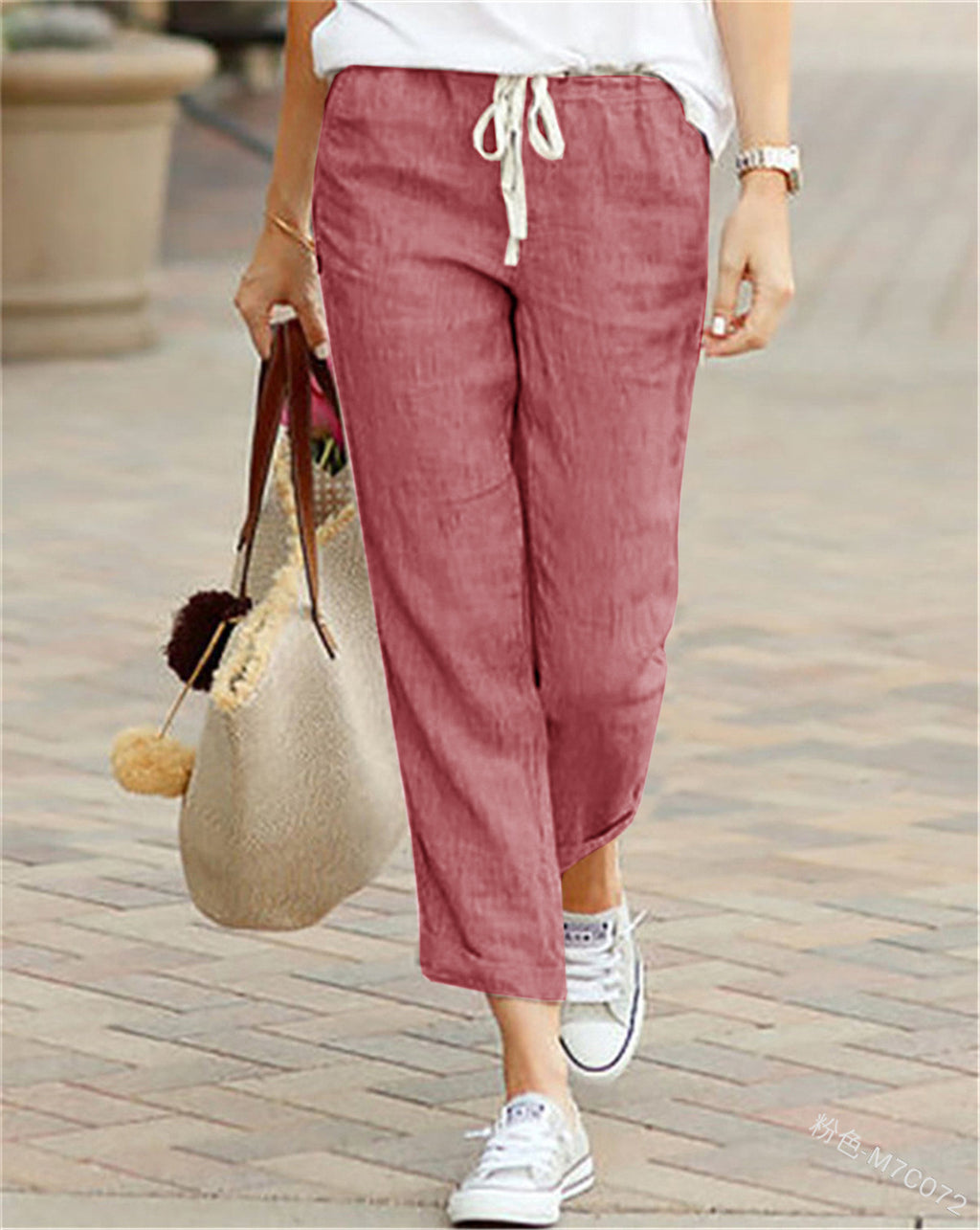Person wearing maroon pants and white sneakers, holding a straw bag on a paved walkway.