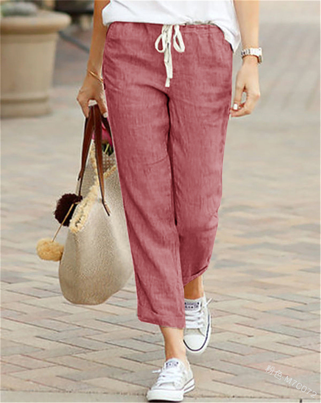 Person wearing maroon pants and white sneakers, holding a straw bag on a paved walkway.