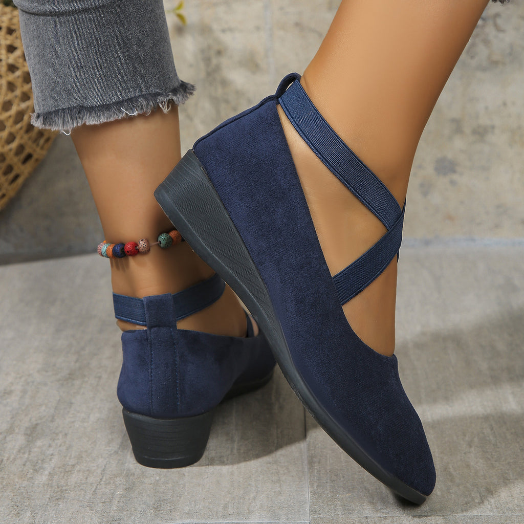 Navy blue suede shoes with criss-cross straps worn by a person on a neutral background