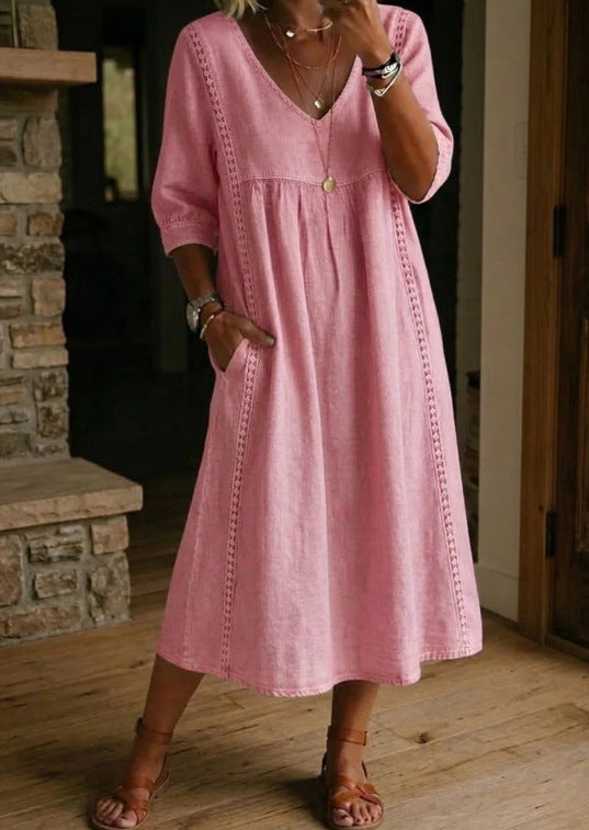 Person wearing a pink dress standing in a room with wooden flooring and a stone wall.
