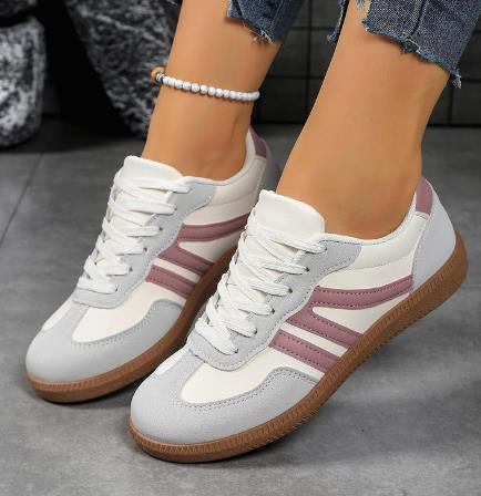 White sneakers with purple stripes worn by a person on a gray floor.