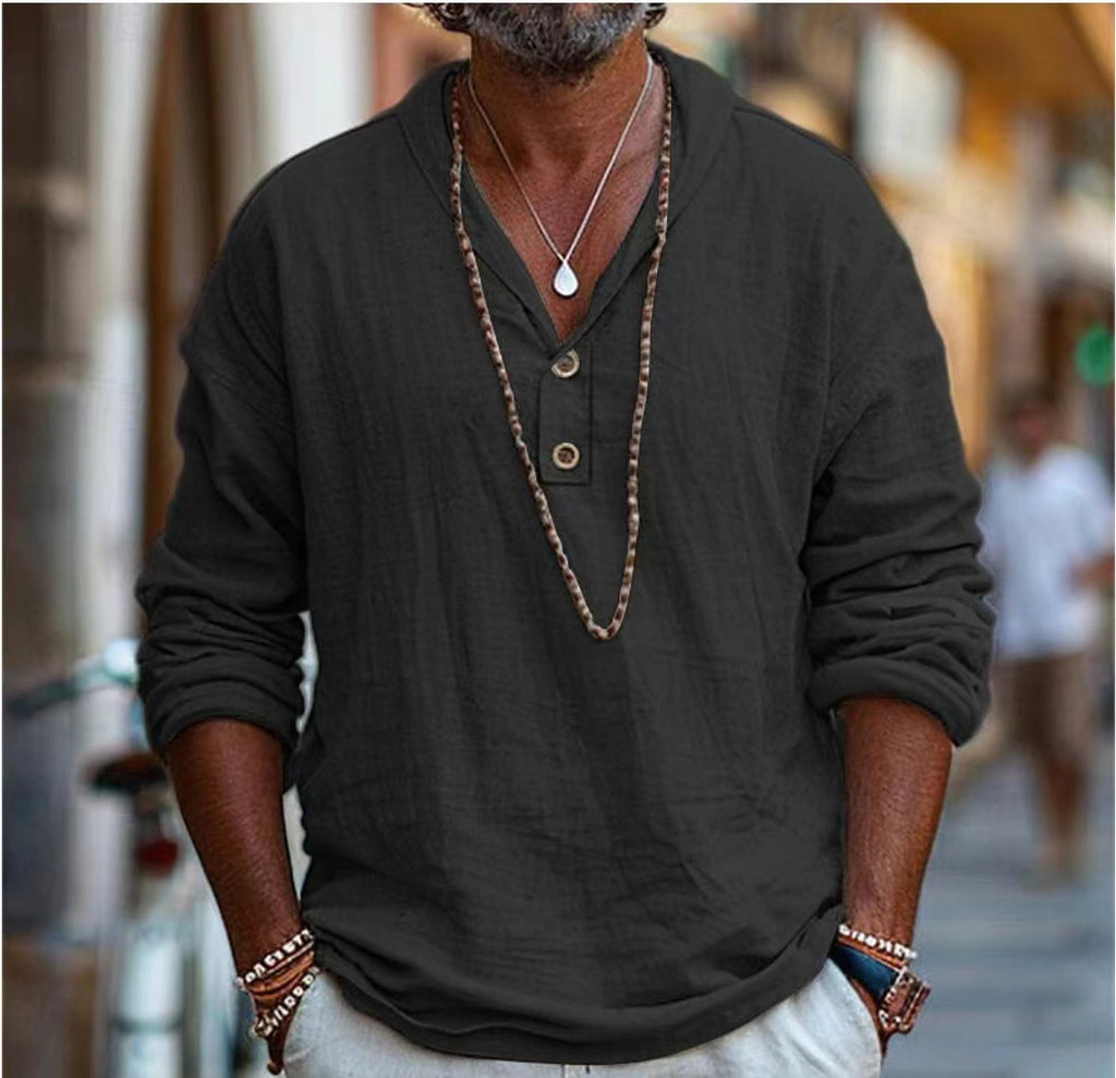 Man wearing a dark long-sleeve shirt with buttons and a necklace, standing outdoors.