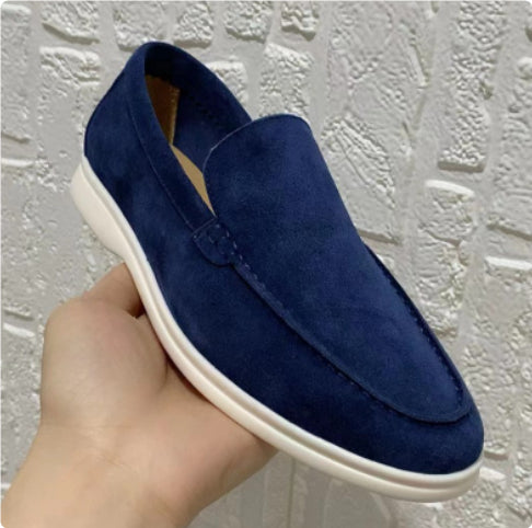 Blue suede loafer shoe held against a textured white background