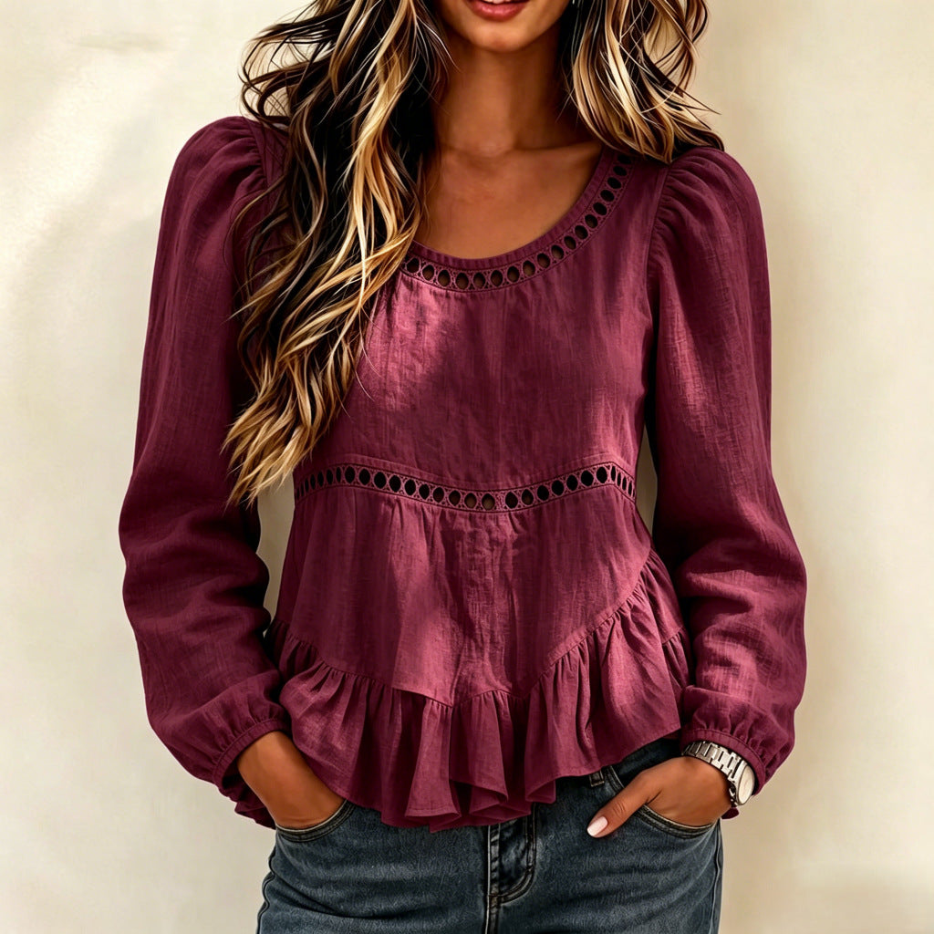 A woman wearing a long-sleeve burgundy peplum blouse with eyelet cutout details, paired with dark blue jeans, standing against a neutral beige background.