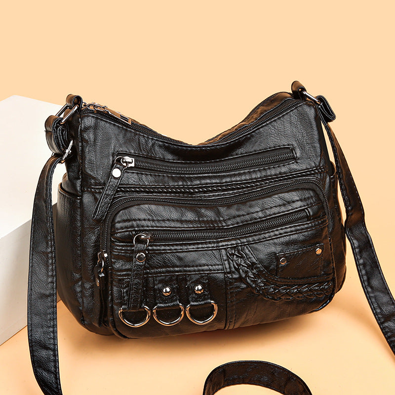 Black leather handbag with multiple zippers on a beige background