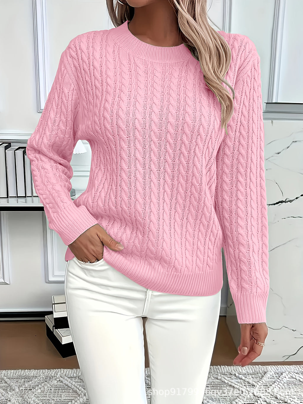 Person wearing a pink cable knit sweater and white pants in an indoor setting.