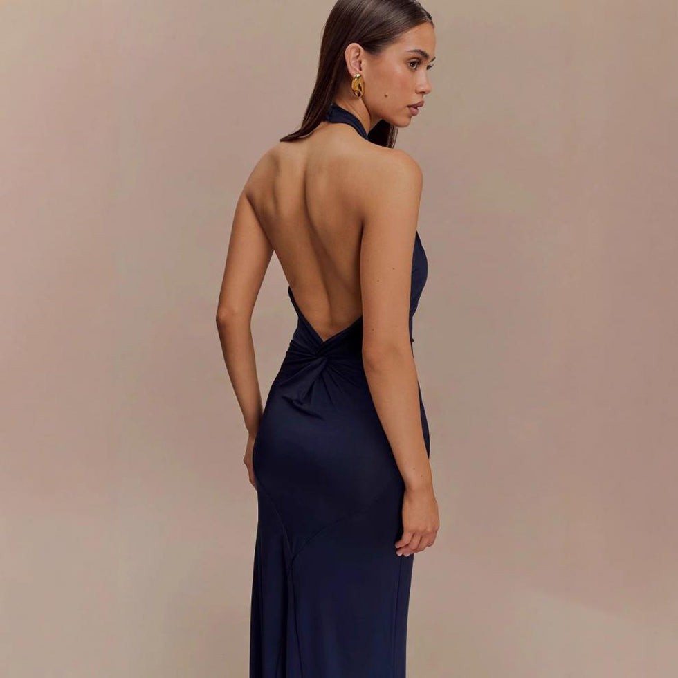 Woman wearing a navy blue evening gown with an open back against a beige background