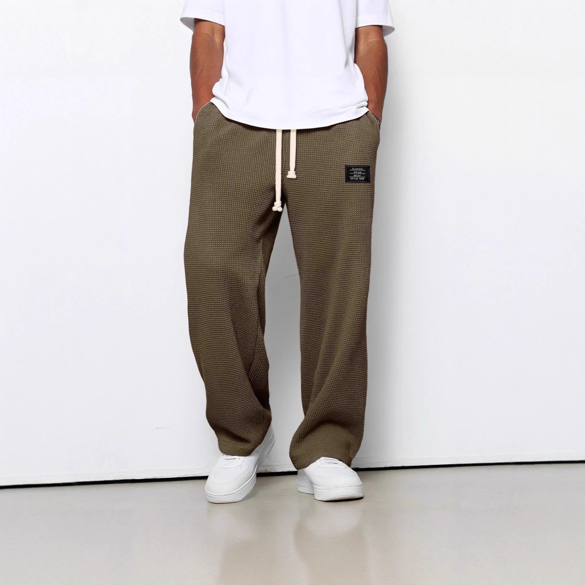 Person wearing brown checkered pants with a white shirt and white shoes on a white background