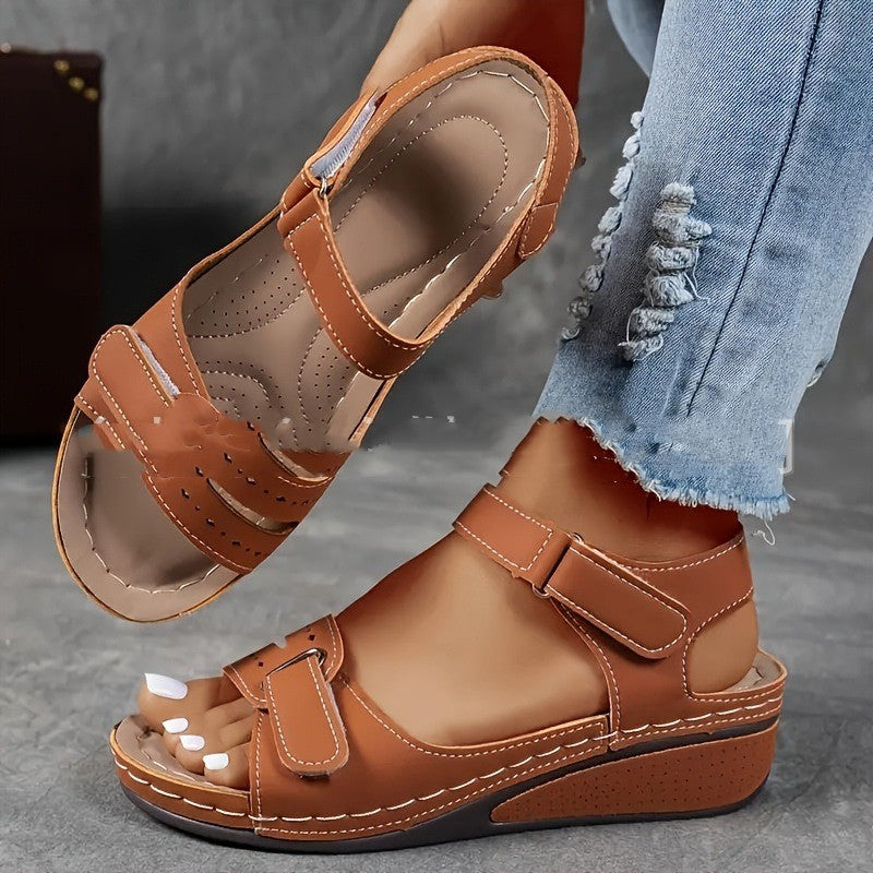 Brown sandals worn with ripped jeans on a gray surface