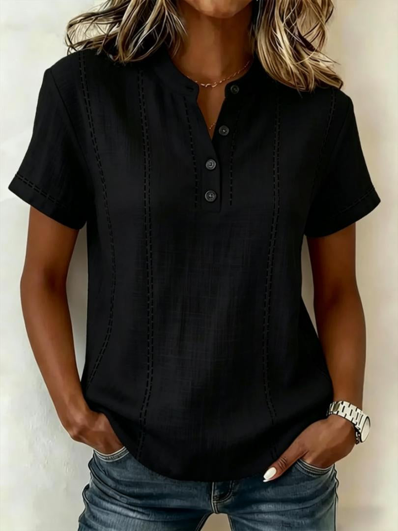 Person wearing a black short-sleeve shirt with buttons, standing against a plain background.
