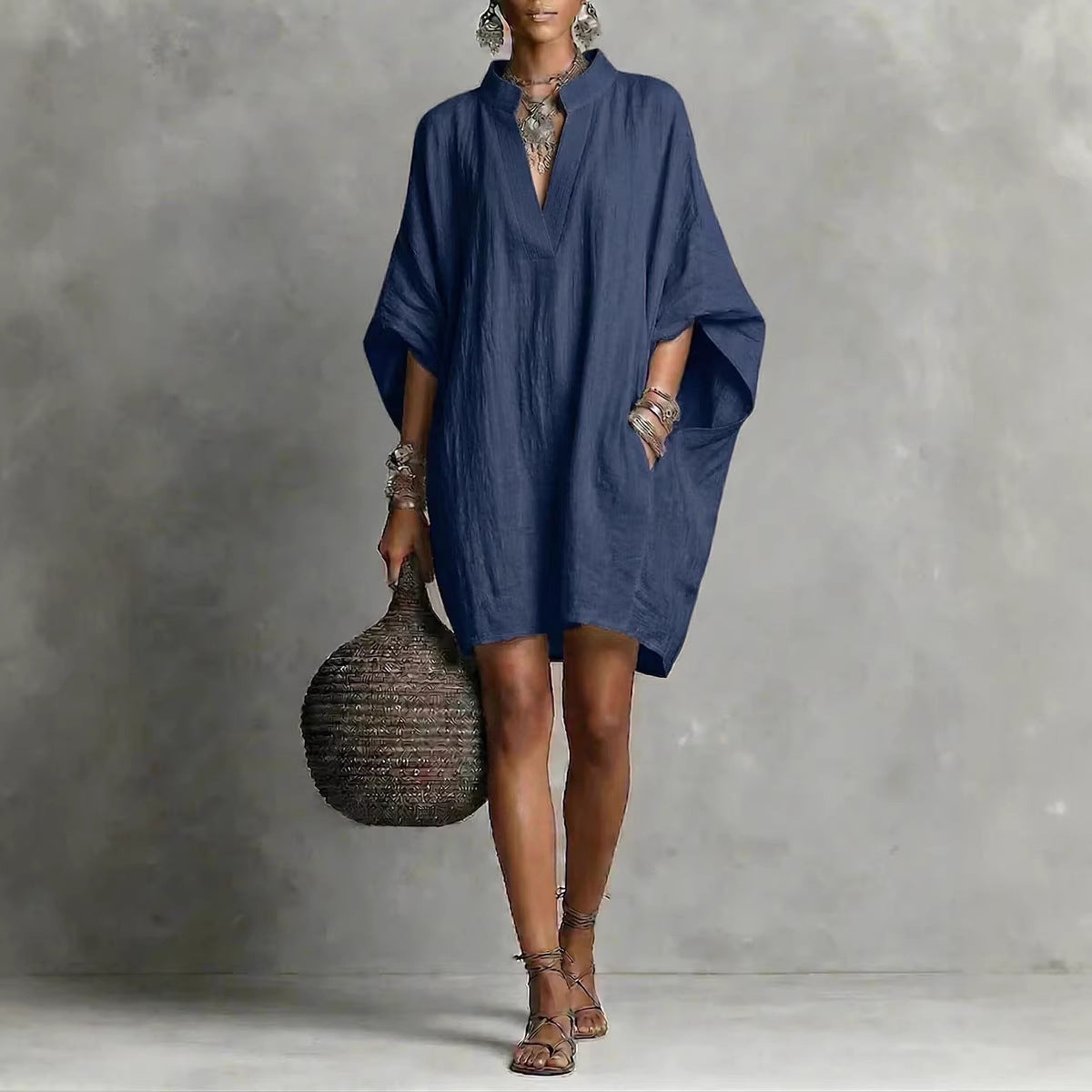 Woman wearing a blue dress holding a textured bag against a gray background
