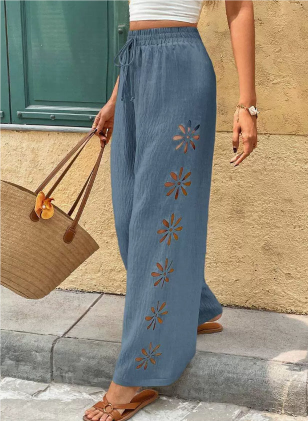 Person wearing blue pants with floral cutouts, standing against a stone wall.