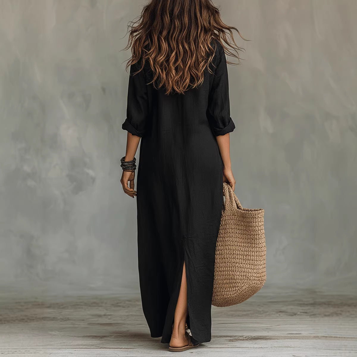 Person wearing a black dress holding a woven bag against a gray wall.