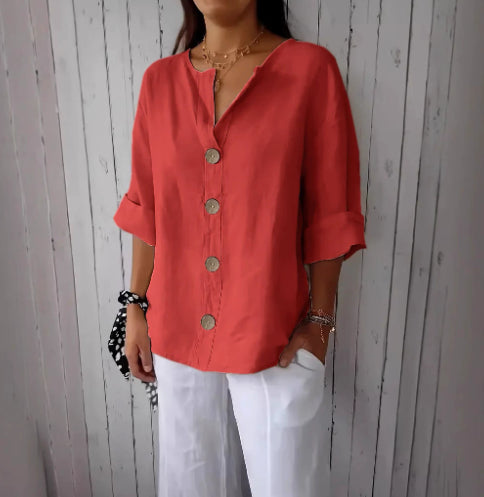 Person wearing a coral button-up shirt and white pants against a wooden paneled wall.