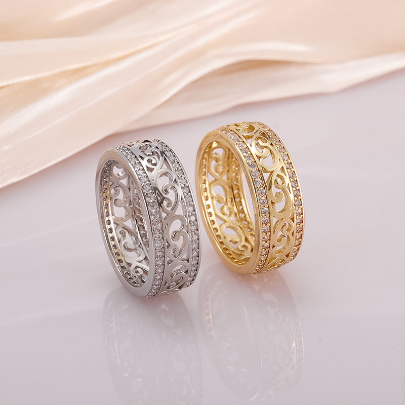 Two intricately designed wedding bands, one gold and one silver, on a soft pink fabric background.