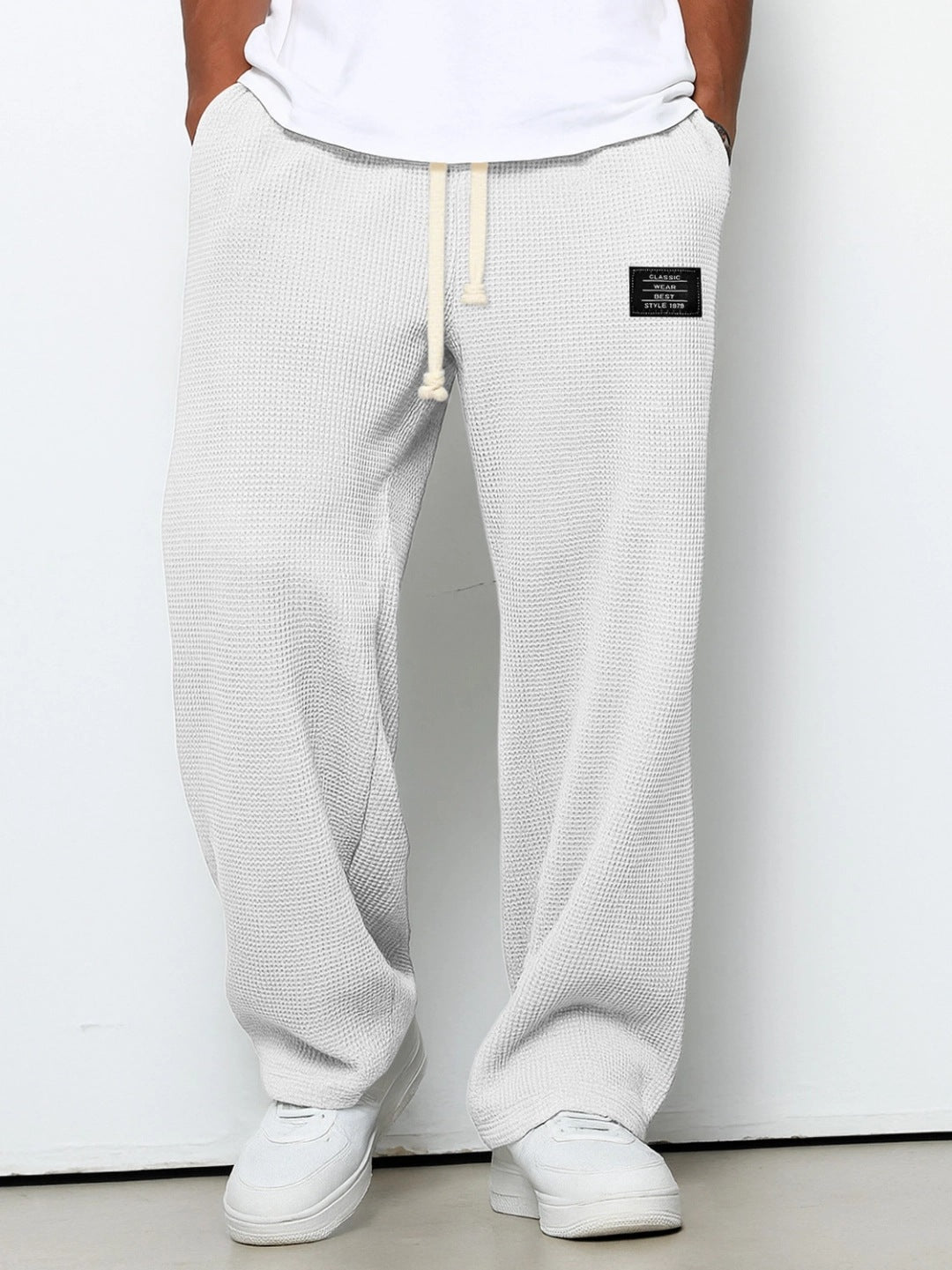 Person wearing light gray textured sweatpants with a brand logo on a white background