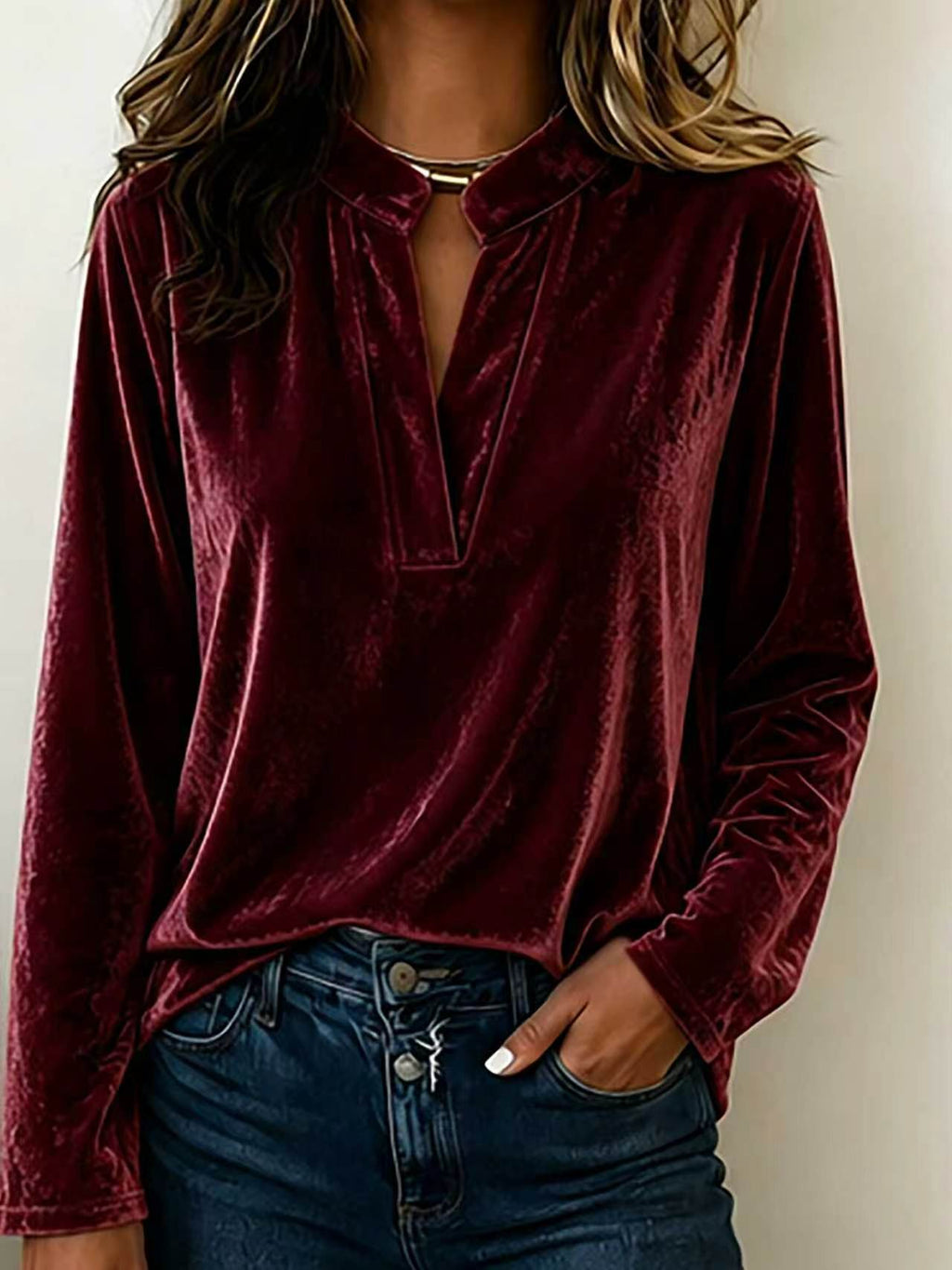 A woman wearing a long-sleeve velvet top in deep burgundy with a split neckline and dark blue jeans, shown from the shoulders to the hips against a plain light background.