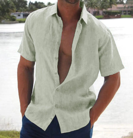 Man wearing a light green shirt with short sleeves, standing by a body of water.