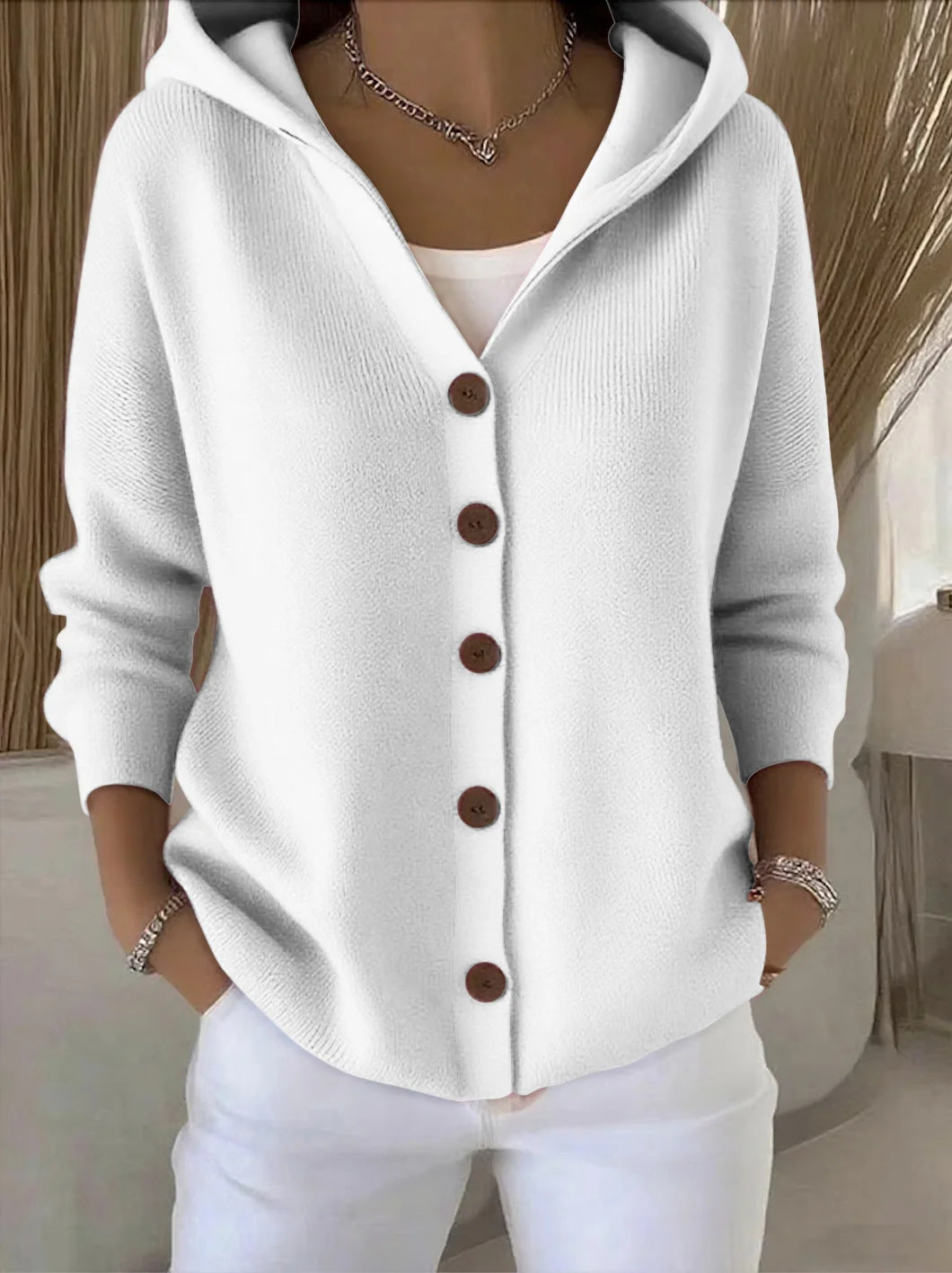 White cardigan with brown buttons worn by a person indoors.