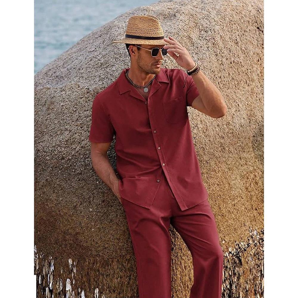 Man in a red outfit and straw hat leaning against a rock by the water.