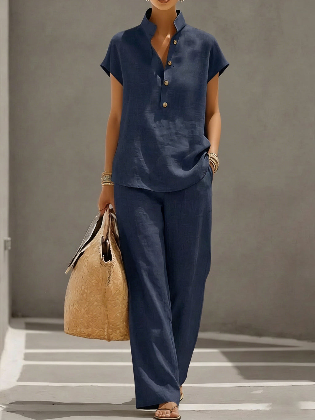 Person wearing a navy blue outfit holding a straw bag on a gray background